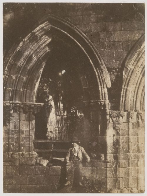 View of a boy sitting on ledge under the ruins of an arched window, England