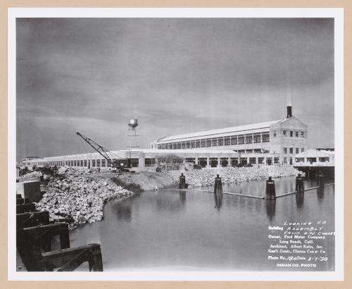 View of the south and east façades of the Assembly Building from the railroad bridge with a dock in the foreground under construction, Ford Motor Company Automobile Assembly Plant, Long Beach, California
