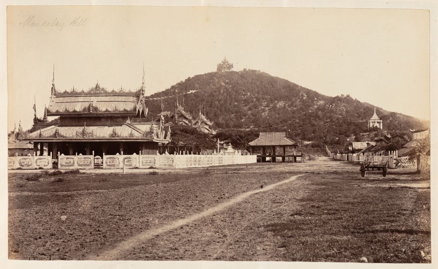 View of Mandalay Hill and a temple with buildings in the foreground, Burma (now Myanmar)