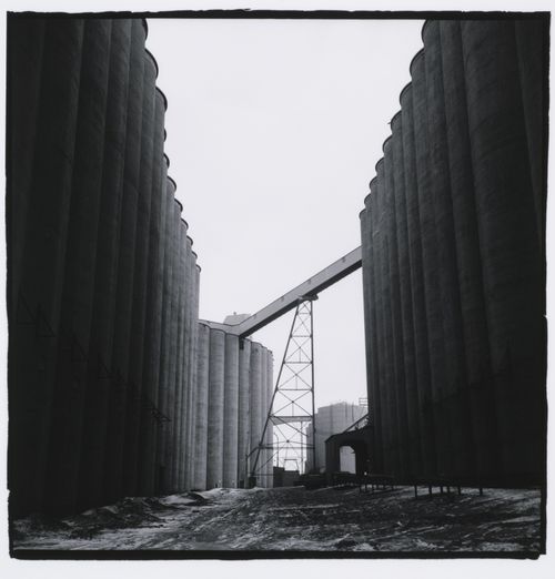 Looking down corridor between rows of tall tube- shaped grain elevators, Minneapolis, Minnesota