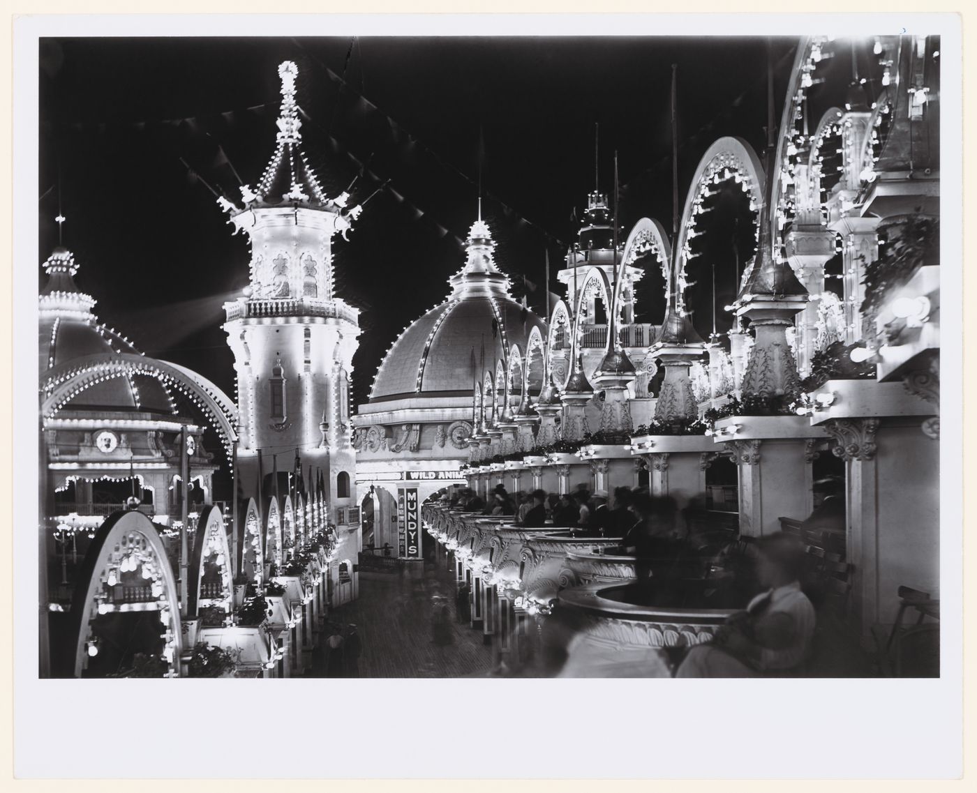 Rows of balconies with seated people on right, people below, admidst [sic] lit arches and buildings at night, Luna Park, Coney Island, New York City, New York