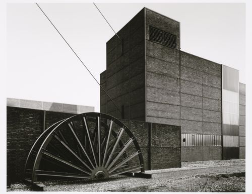 View of a mine building of Zeche Zollverein Pit No. 12 [Colliery Zollverein Pit No. 12] with a half-wheel of a minehead in the foreground, Stoppenberg and Katernberg, Essen, Germany