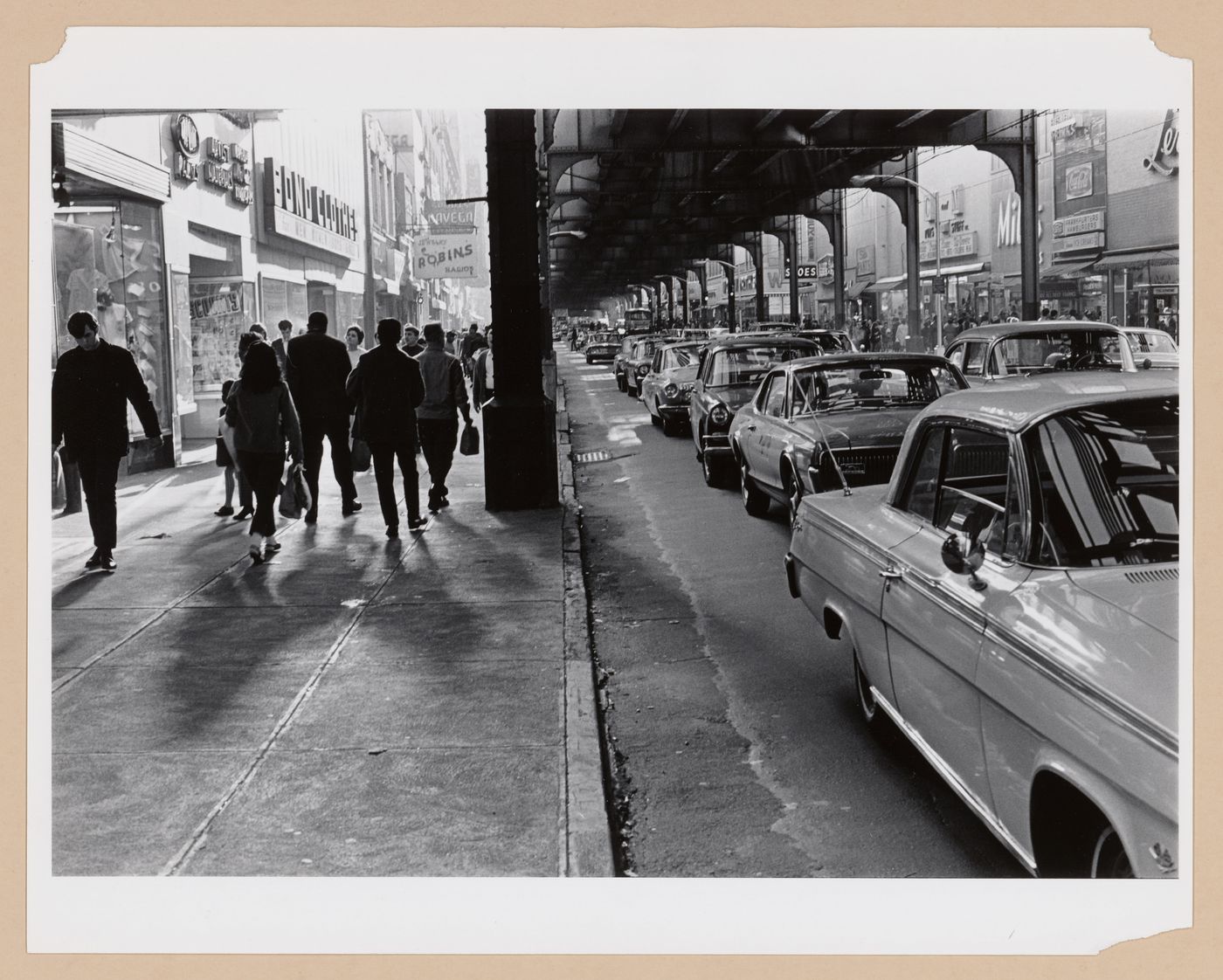 View of Jamaica Avenue showing people walking on the sidewalk and cars stopped in a traffic jam under an elevated subway line, Long Island, United States