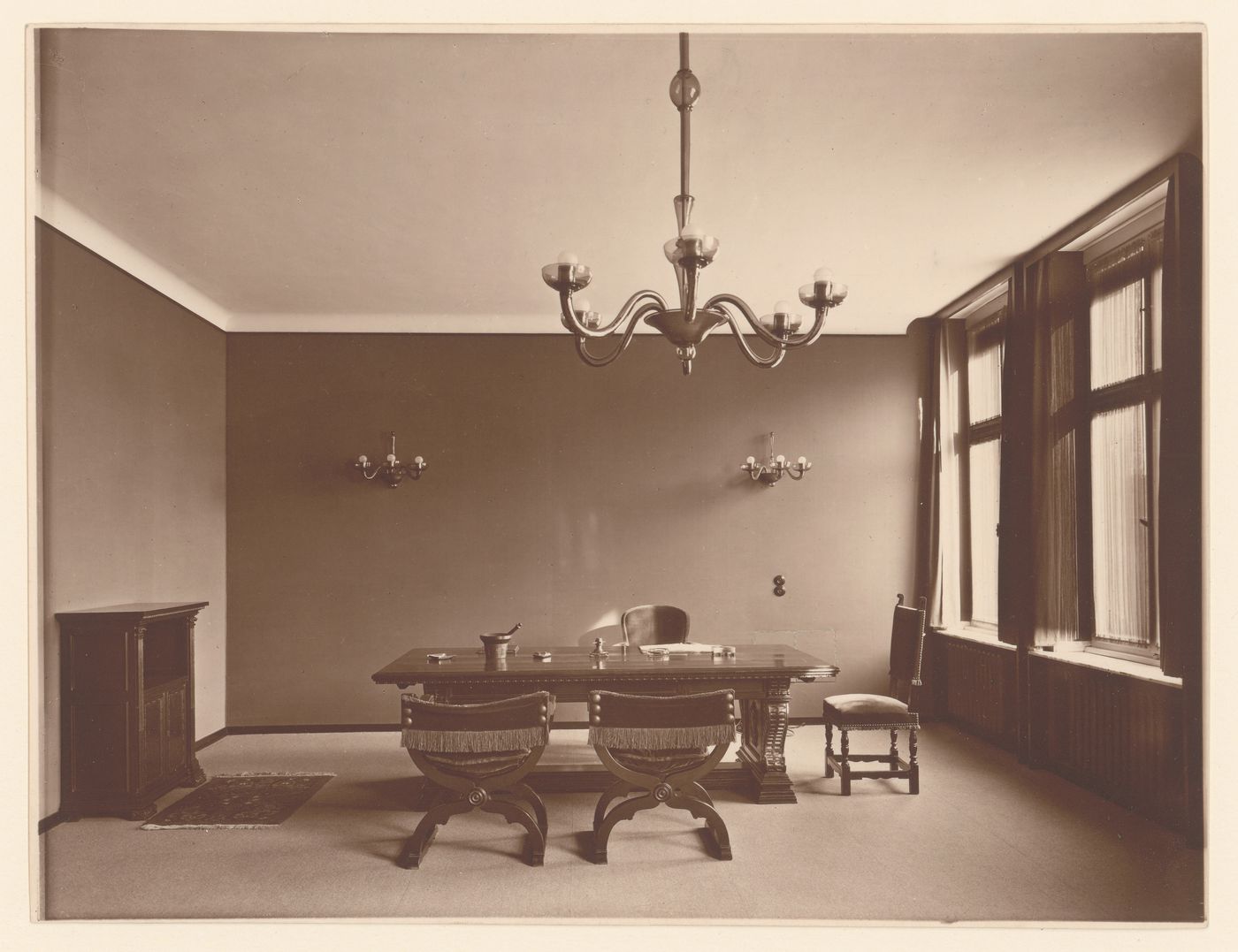 Interior, unidentified house, work room with large table, fireplace, chandelier, and chairs with fringed backs