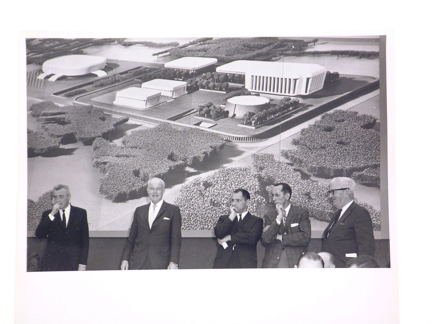 View of the dedication ceremony of the John F. Kennedy Educational, Civic and Cultural Center showing a photograph of the model of the building and five men on the platform, Mineola, New York