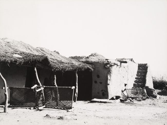 Rural dwellings with traditional charpai, a light bedstead, prominenty visible