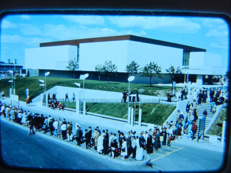 Vue du pavillon de l'Homme créateur avec, au premier plan, des visiteurs faisant la queue à un arrêt de train à remorque, Expo 67, Montréal, Québec