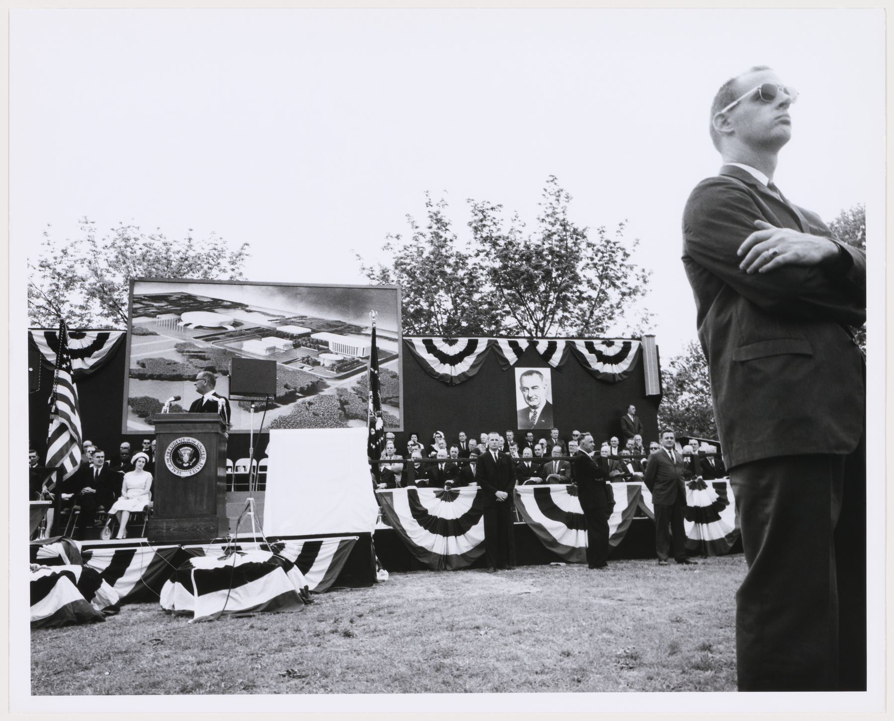 Ben Schnall, View of the dedication ceremony of the John F. Kennedy Educational Civic, and Cultural Center showing a partial view of the platform with people and a photograph of the model of the building, Mineola, New York, 1968