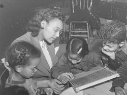 Des enfants, assis autour d'une table, tissent à l'aiguille avec l'aide d'une éducatrice