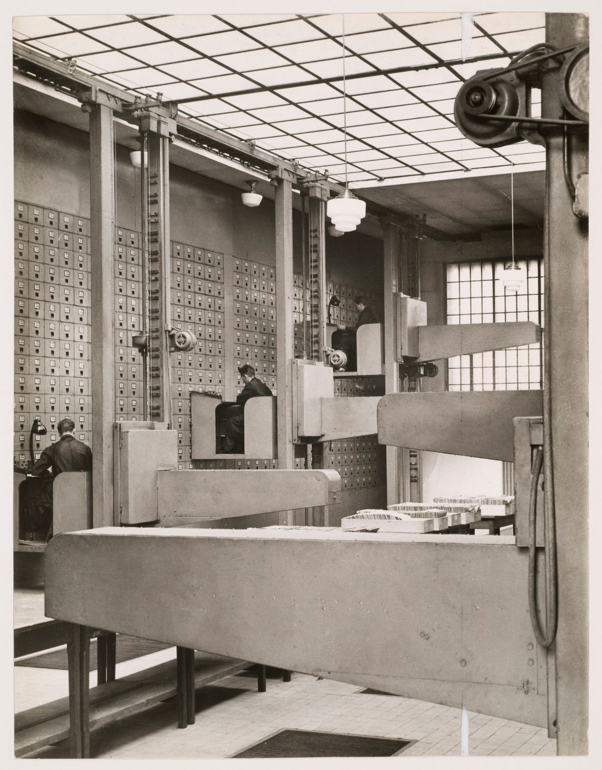 interior view of the Central Social Insurance Institution showing men working in mobile work stations used to access the card catalog drawers
